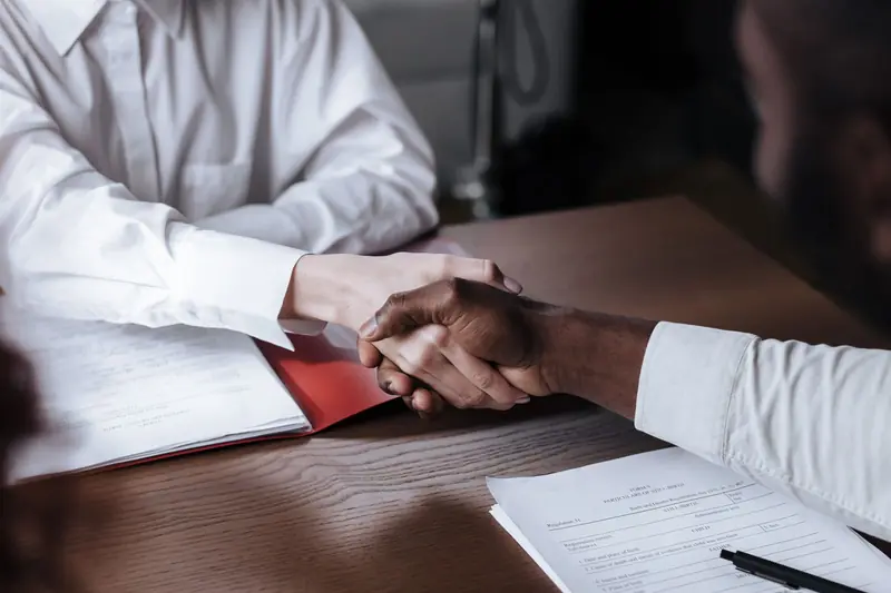 Two business people shaking hands over contract documents
